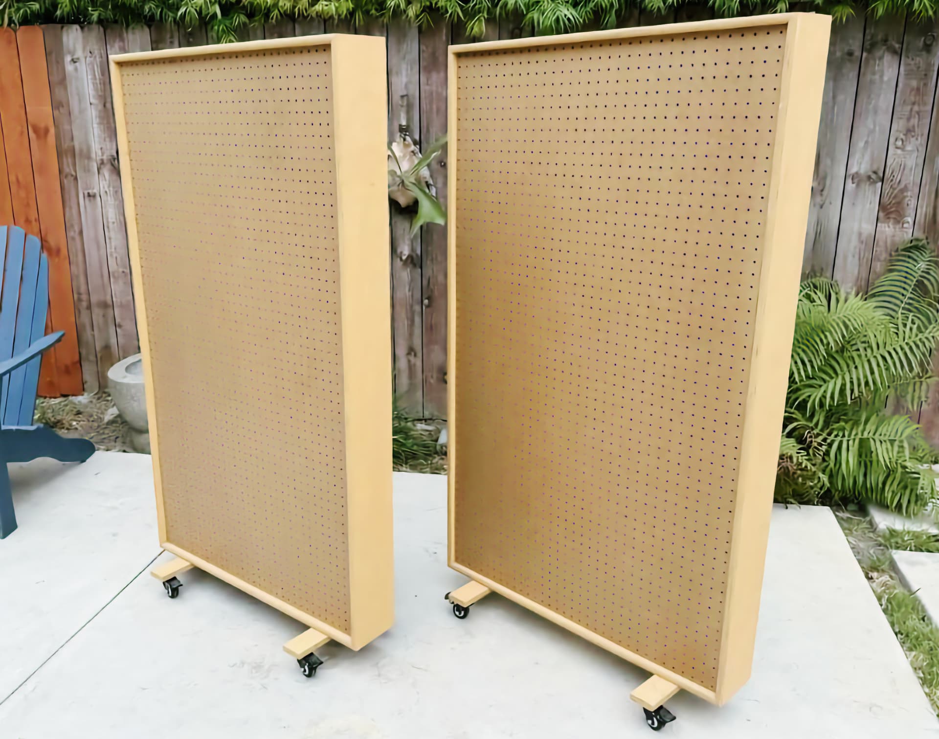 A pair of tall perforated-hardboard acoustic gobos in maple frames, standing on locking casters on a patio.
