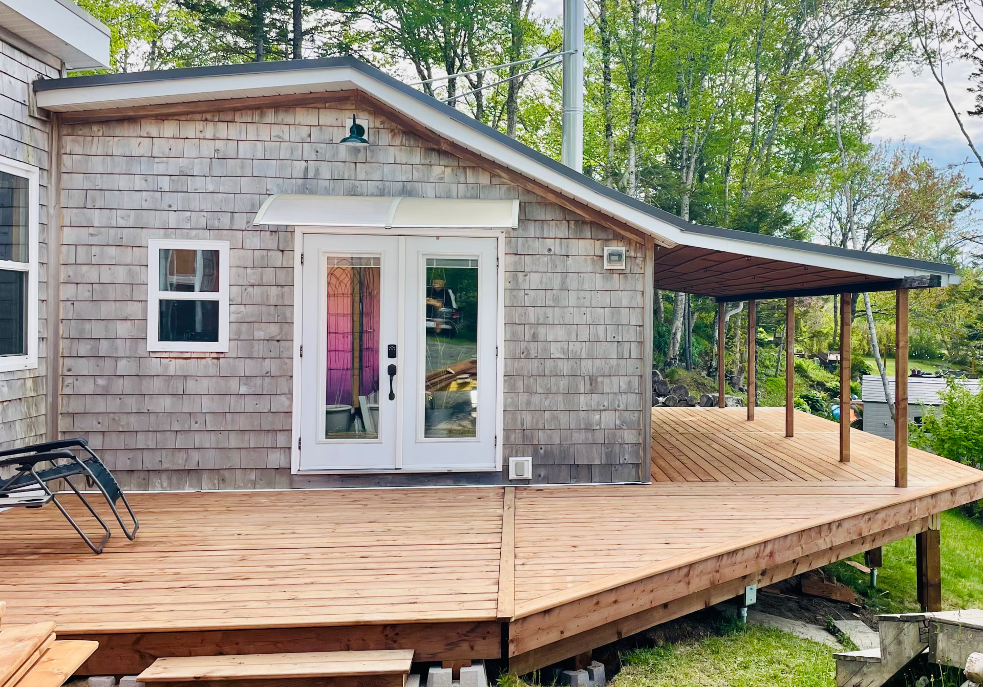 A new wood deck wrapping a shingled house, with a covered section supported by square posts.