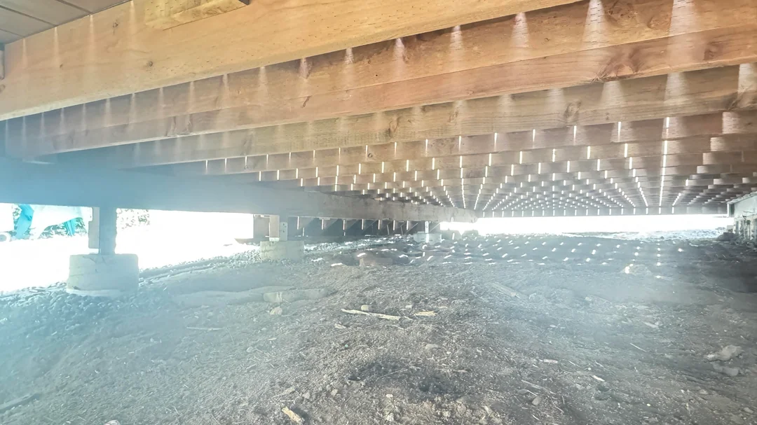 The underside of a deck showing joists, beams and concrete pier footings with daylight between the boards.
