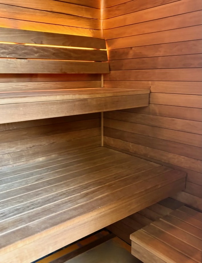 Warmly lit tiered cedar benches inside a finished sauna, with a backrest and concealed light strip along the wall.